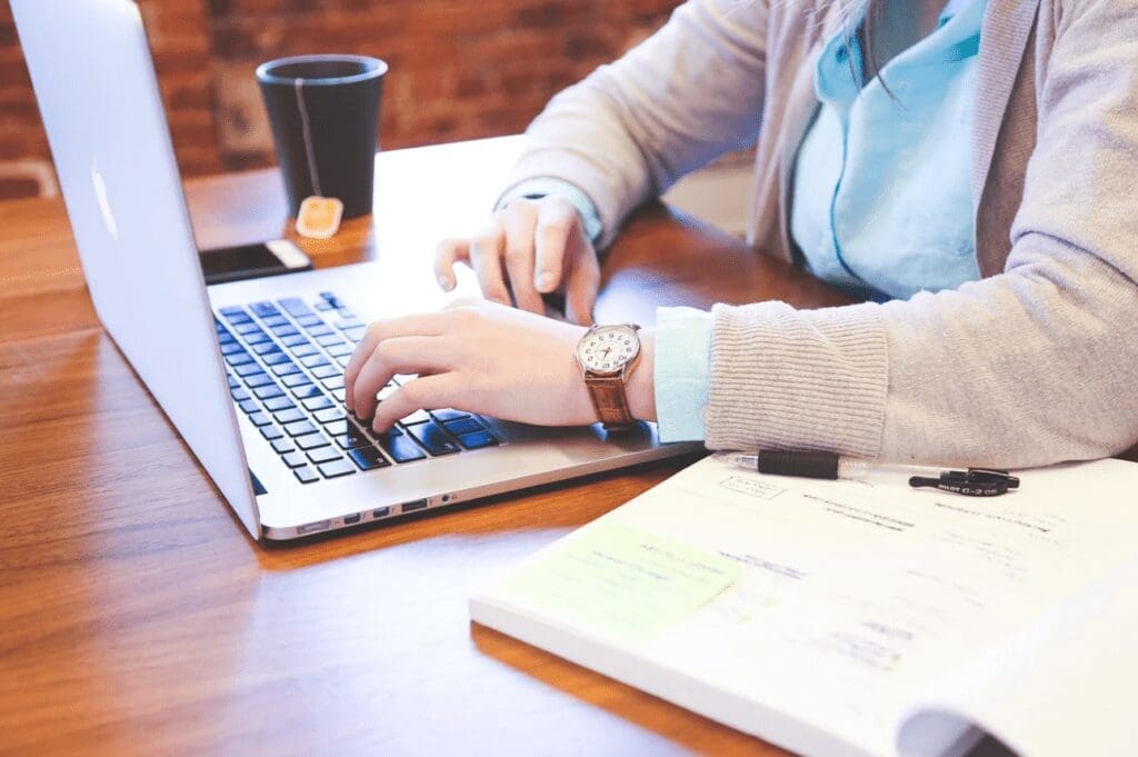 A woman working on a laptop with a notebook and pen, coffee and mobile next to her