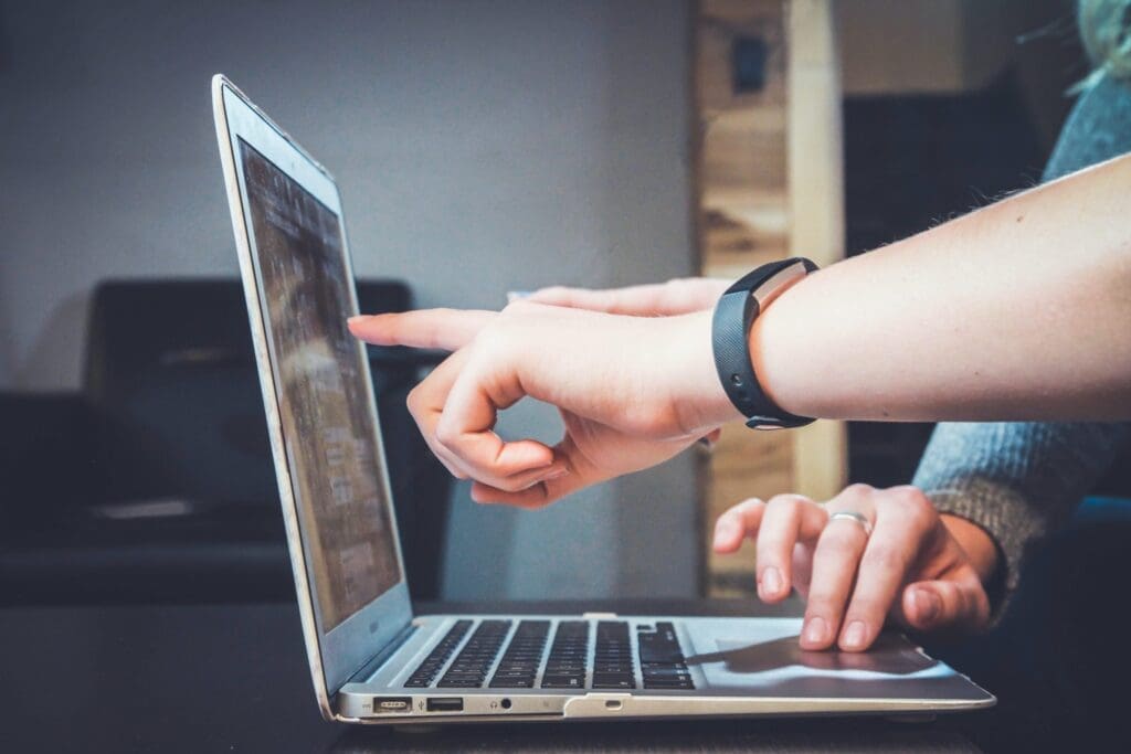 Laptop with hands pointing at the screen, and another hand navigating the laptop